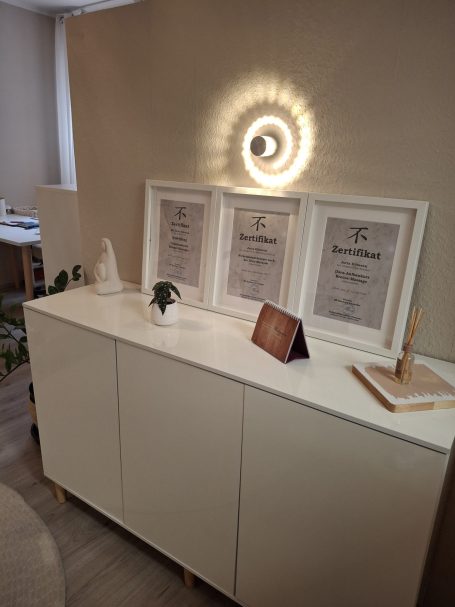 Weißer Schrank mit gerahmten Dokumenten und dekorativen Objekten im Hintergrund.