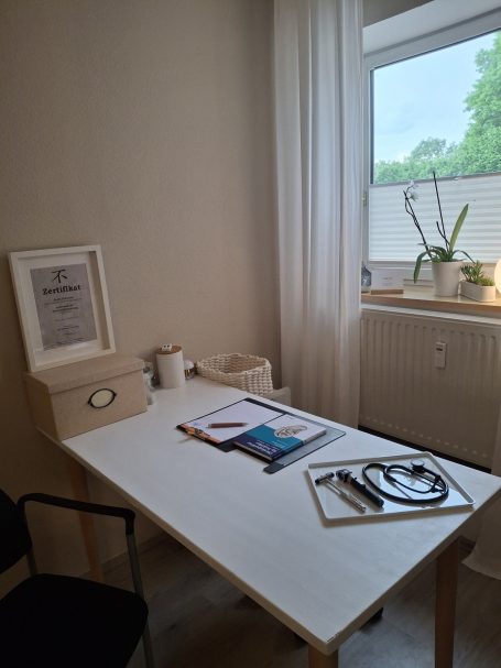 Heller Raum mit einem Tisch, Stuhl, Pflanzen und Unterlagen auf dem Tisch.