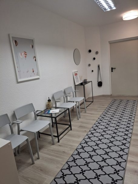 Wartebereich mit grauen Stühlen, Tisch und graphischen Wanddekorationen.